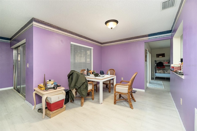 dining area featuring a textured ceiling, light hardwood / wood-style flooring, and ornamental molding