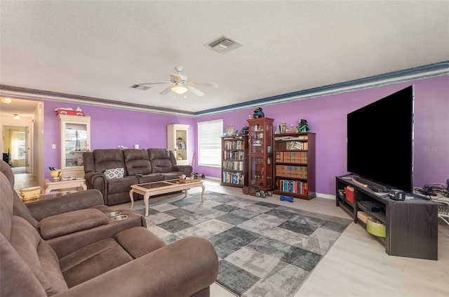 living room with a textured ceiling, wood finished floors, visible vents, a ceiling fan, and ornamental molding