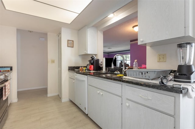 kitchen featuring dark stone counters, a sink, white cabinets, light wood-type flooring, and dishwasher