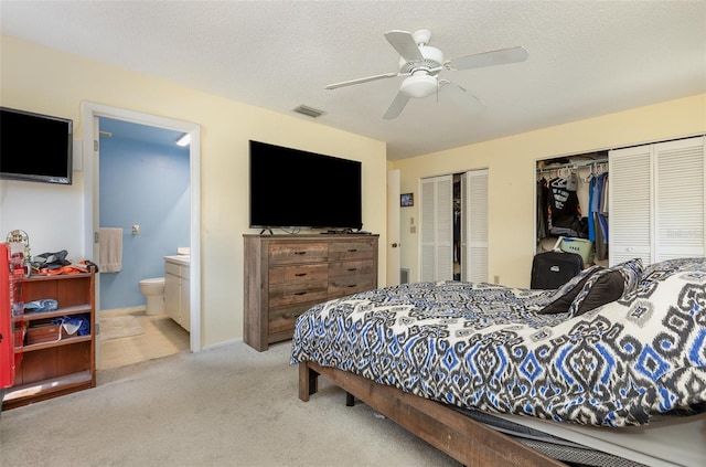 bedroom with carpet, multiple closets, visible vents, connected bathroom, and a textured ceiling