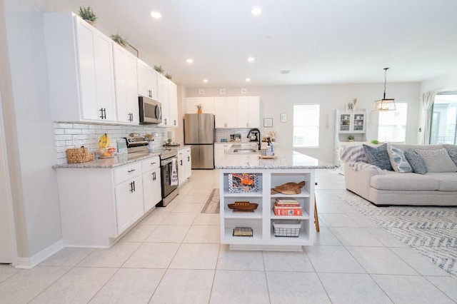 kitchen with sink, white cabinetry, stainless steel appliances, a center island with sink, and decorative light fixtures