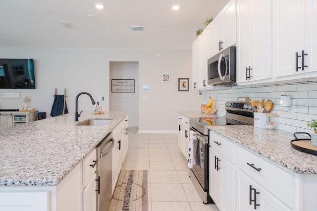 kitchen with sink, light tile patterned floors, appliances with stainless steel finishes, an island with sink, and white cabinets