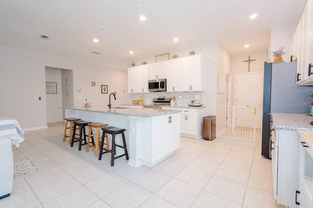 kitchen featuring stainless steel appliances, white cabinetry, light stone countertops, and a center island with sink