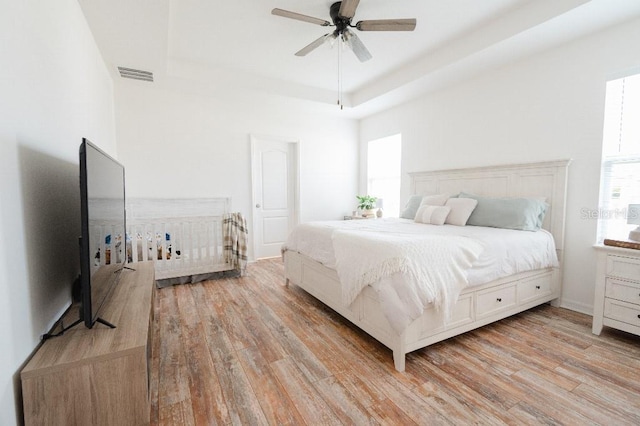 bedroom with light wood-type flooring, ceiling fan, and a tray ceiling