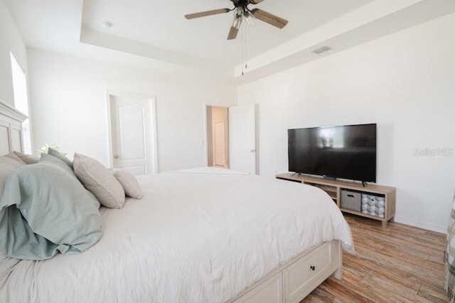 bedroom with a tray ceiling, ceiling fan, and light wood-type flooring