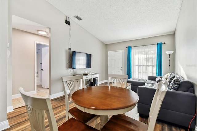 dining room featuring vaulted ceiling, light hardwood / wood-style flooring, and a textured ceiling