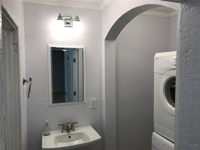 bathroom with crown molding, stacked washer and dryer, and sink