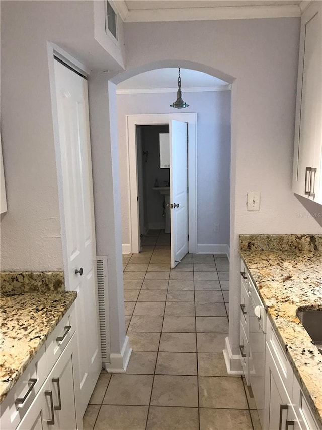 kitchen with white cabinetry, ornamental molding, light stone counters, and light tile patterned floors