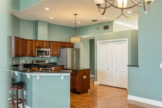 kitchen with stainless steel appliances, hanging light fixtures, a kitchen bar, and dark stone counters