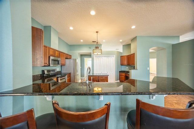 kitchen with appliances with stainless steel finishes, kitchen peninsula, hanging light fixtures, and dark stone countertops