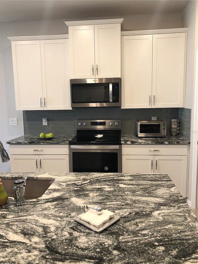 kitchen featuring backsplash, white cabinetry, appliances with stainless steel finishes, and dark stone countertops