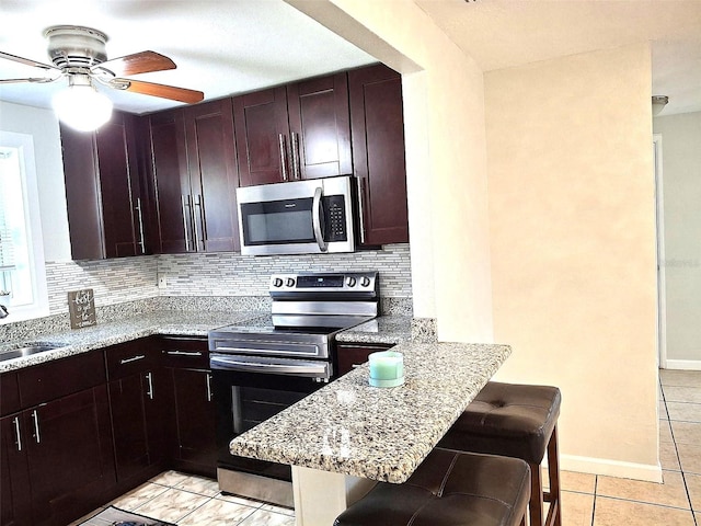 kitchen with stainless steel appliances, light stone countertops, a breakfast bar, and decorative backsplash