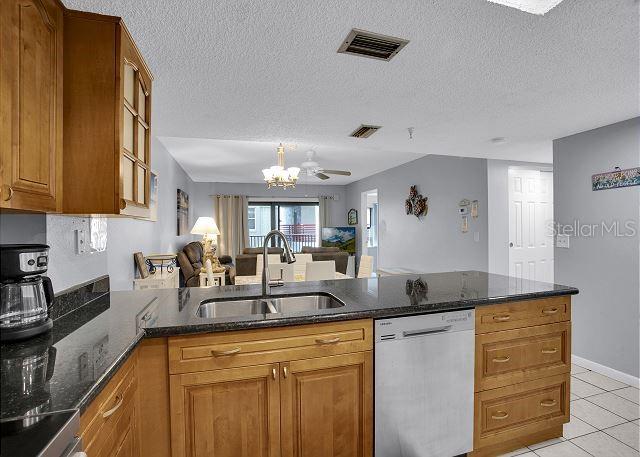 kitchen with light tile patterned flooring, sink, stainless steel dishwasher, kitchen peninsula, and a textured ceiling