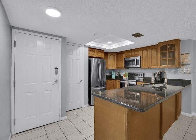 kitchen with sink, light tile patterned floors, kitchen peninsula, stainless steel appliances, and a textured ceiling