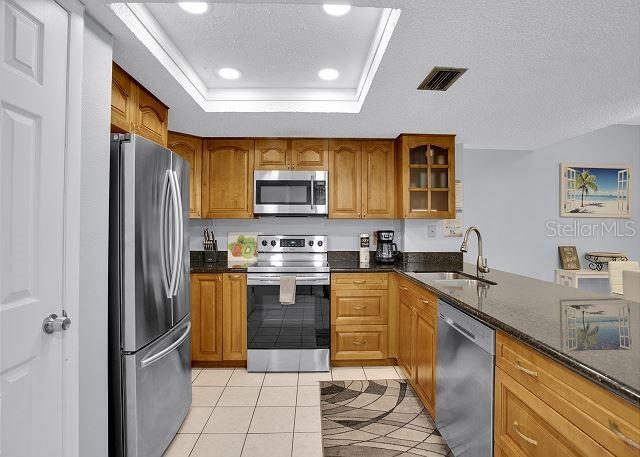 kitchen featuring light tile patterned flooring, appliances with stainless steel finishes, sink, dark stone countertops, and a tray ceiling