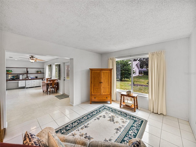 living room featuring ceiling fan, light tile patterned floors, and a textured ceiling