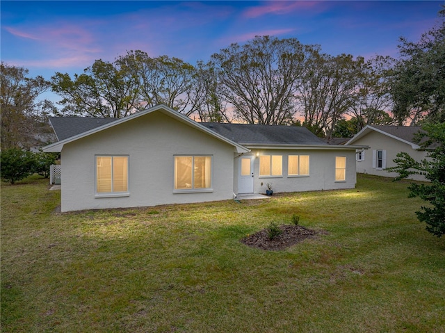 back house at dusk featuring a lawn