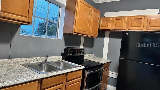 kitchen featuring ornamental molding, black refrigerator, sink, and electric range