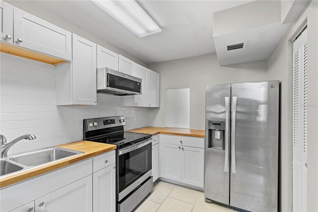 kitchen featuring butcher block countertops, appliances with stainless steel finishes, white cabinetry, backsplash, and light tile patterned flooring