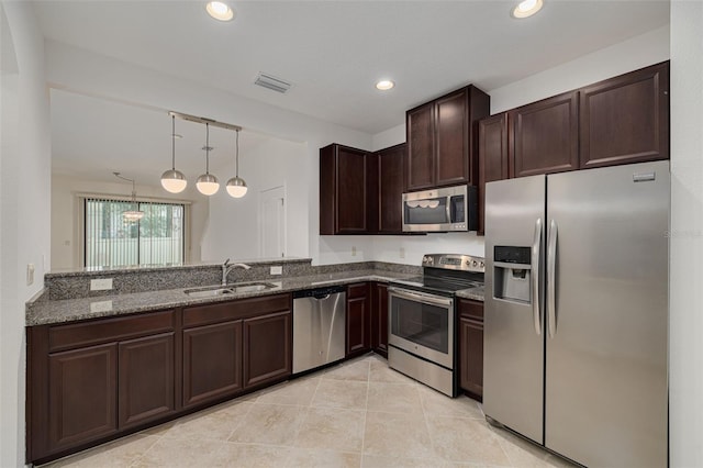 kitchen featuring pendant lighting, appliances with stainless steel finishes, dark stone countertops, sink, and dark brown cabinets