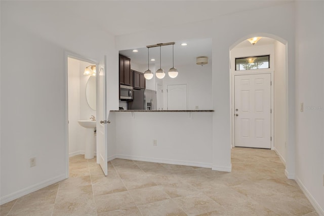 kitchen featuring kitchen peninsula, dark brown cabinets, pendant lighting, appliances with stainless steel finishes, and dark stone counters