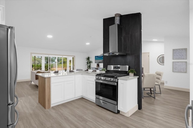 kitchen featuring wall chimney exhaust hood, appliances with stainless steel finishes, a peninsula, light countertops, and white cabinetry