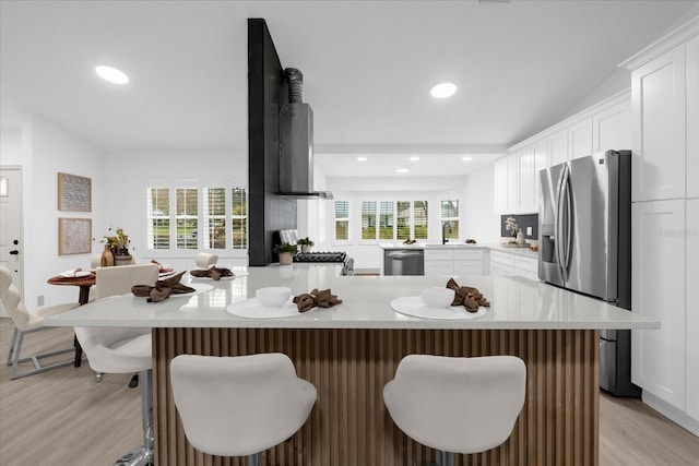 kitchen with a breakfast bar, range hood, white cabinets, kitchen peninsula, and stainless steel appliances