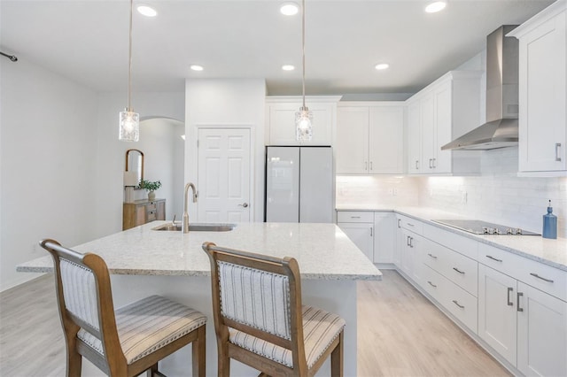 kitchen with wall chimney range hood, sink, hanging light fixtures, black electric stovetop, and white fridge