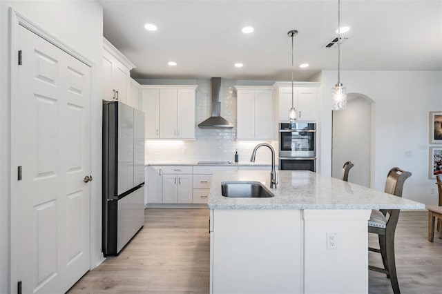 kitchen featuring pendant lighting, sink, white cabinets, stainless steel appliances, and wall chimney range hood