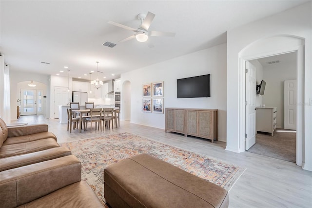 living room featuring ceiling fan with notable chandelier and light hardwood / wood-style flooring