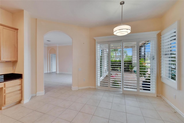 unfurnished dining area featuring light tile patterned floors, baseboards, and arched walkways