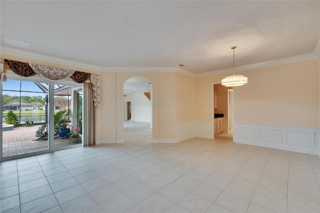 spare room featuring arched walkways, light tile patterned floors, a decorative wall, and crown molding