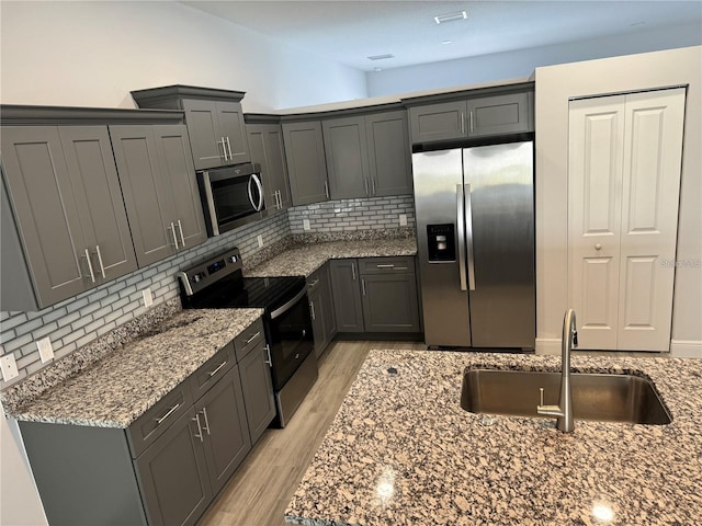 kitchen featuring appliances with stainless steel finishes, decorative backsplash, sink, stone countertops, and light wood-type flooring