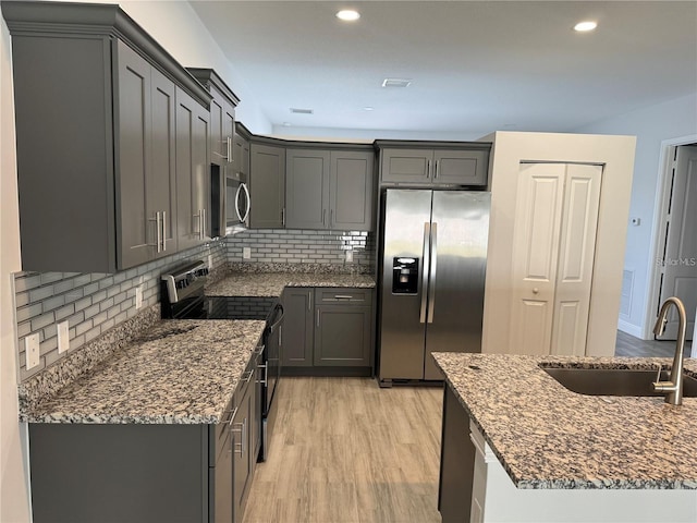 kitchen with stainless steel appliances, dark stone counters, light hardwood / wood-style floors, sink, and gray cabinets