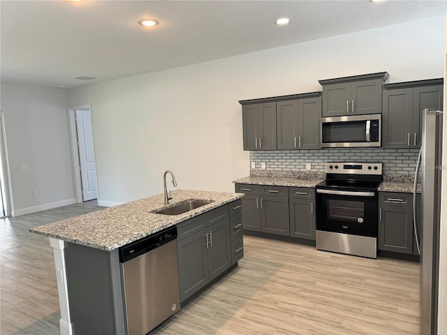 kitchen featuring light hardwood / wood-style flooring, appliances with stainless steel finishes, sink, light stone countertops, and an island with sink