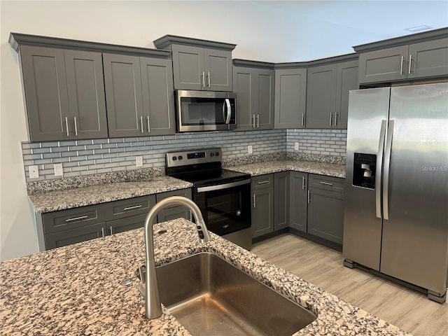 kitchen with sink, backsplash, light wood-type flooring, light stone counters, and stainless steel appliances