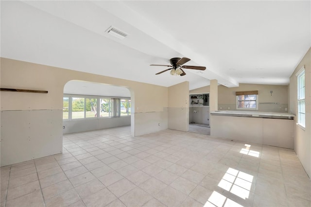 unfurnished living room featuring arched walkways, healthy amount of natural light, a ceiling fan, and light tile patterned floors