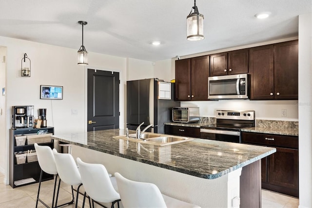 kitchen featuring a kitchen island with sink, sink, stainless steel appliances, and hanging light fixtures