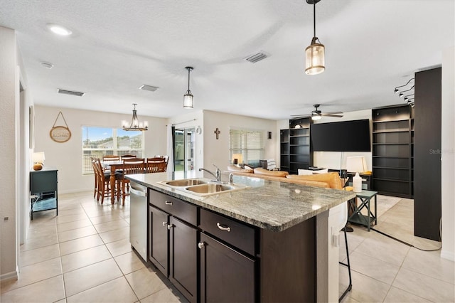 kitchen featuring light tile patterned flooring, sink, light stone counters, decorative light fixtures, and stainless steel dishwasher