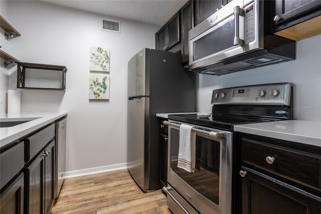 kitchen featuring stainless steel appliances, a textured ceiling, and light hardwood / wood-style flooring