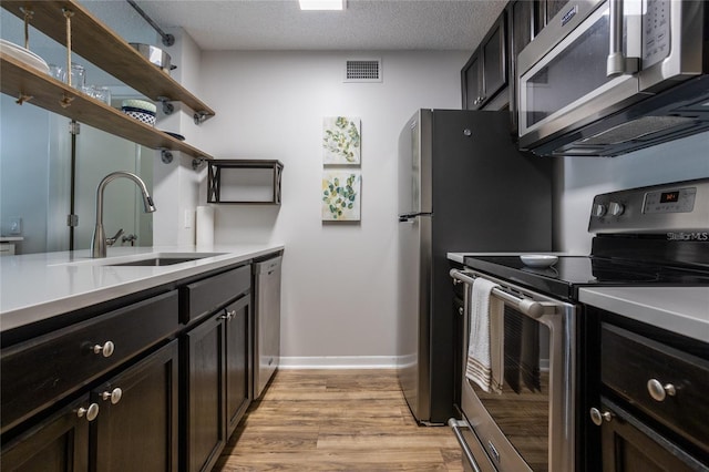 kitchen with appliances with stainless steel finishes, sink, a textured ceiling, and light wood-type flooring