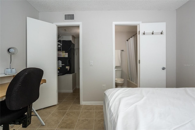 bedroom featuring a spacious closet, tile patterned floors, a textured ceiling, and ensuite bathroom