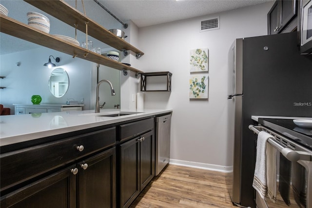 kitchen featuring appliances with stainless steel finishes, sink, light hardwood / wood-style floors, dark brown cabinets, and a textured ceiling