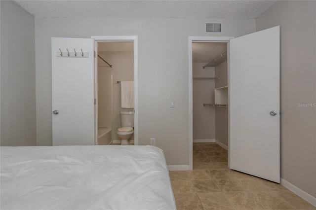 bedroom with a walk in closet, ensuite bathroom, a closet, and a textured ceiling