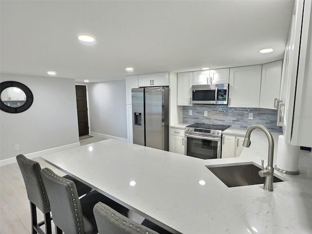 kitchen with sink, a breakfast bar, stainless steel appliances, tasteful backsplash, and white cabinets