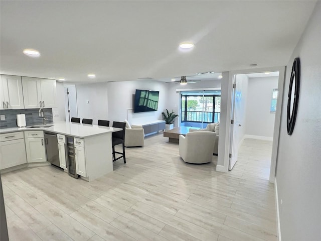 kitchen featuring sink, dishwasher, white cabinetry, backsplash, and a kitchen breakfast bar