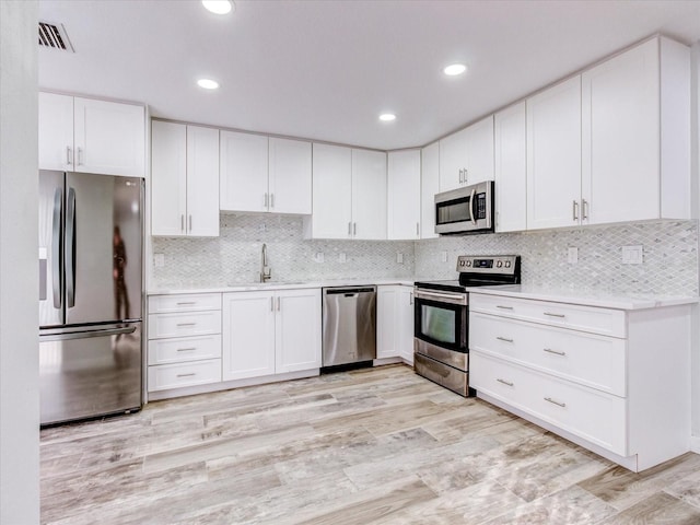 kitchen with stainless steel appliances, sink, white cabinets, and light hardwood / wood-style floors