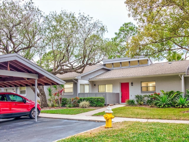 mid-century modern home with roof with shingles, a front yard, and stucco siding