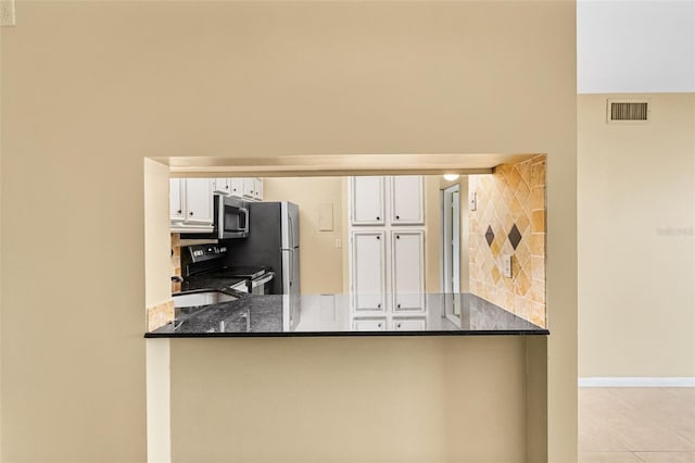 kitchen featuring white cabinetry, backsplash, stainless steel appliances, kitchen peninsula, and dark stone counters