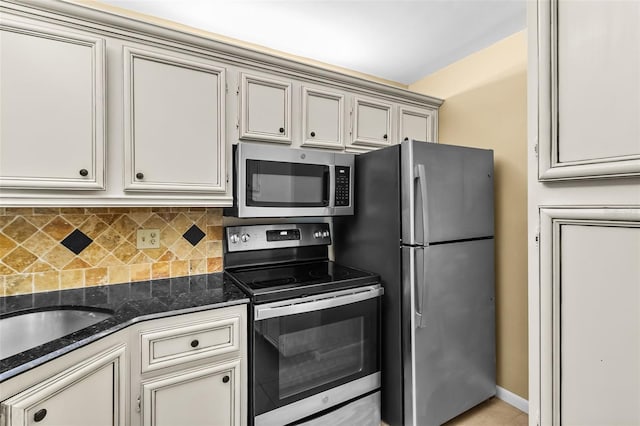 kitchen with appliances with stainless steel finishes, dark stone countertops, backsplash, cream cabinets, and light tile patterned flooring